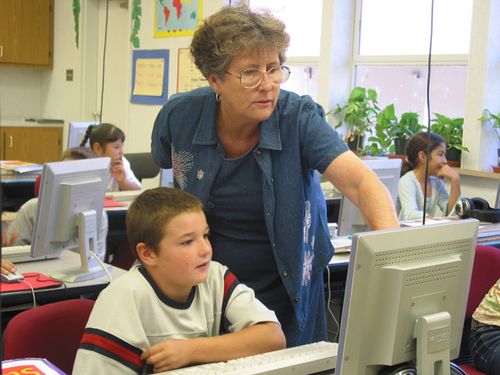 A teacher pointing to a computer screen for a student