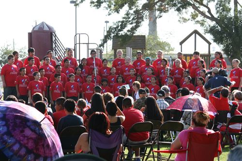 Choir members wearing matching red shirts performing in front of an audience outside